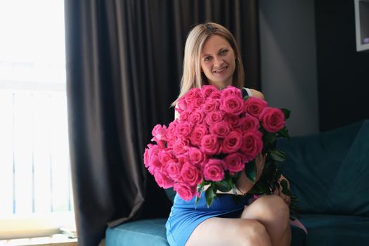 A young woman is sitting on a sofa with a large bouquet of roses, close-up. Romance, holiday greetings, wedding anniversary