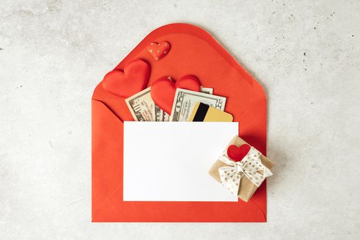 Red paper envelope with blank paper white note mockup. Flat lay of gray working table background with Valentine gift, letter, heart shape, money dollars, credit card. Top view, mock up greeting card