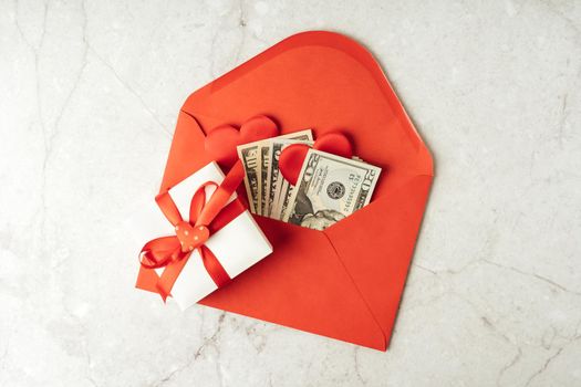 Red paper envelope with money dollars bills. Flat lay of gray working table background with Valentine gift, letter, heart shape. Top view, mock up greeting card. Valentine's Day budget