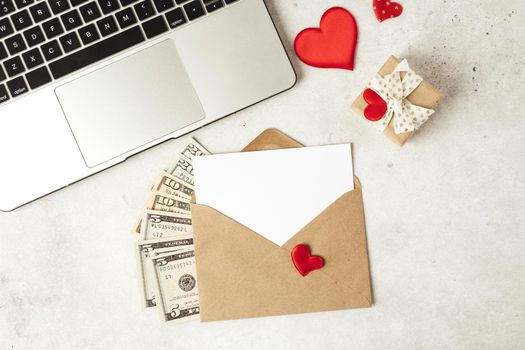 Red paper envelope with blank paper white note mockup. Flat lay of gray working table background with Valentine gift, letter, heart shape, laptop and money dollars. Top view, mock up greeting card