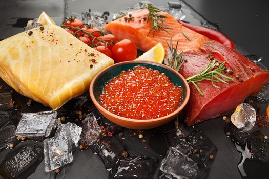 Caviar, smoked salmon, tuna, hausen and vegetables on a black board with ice.