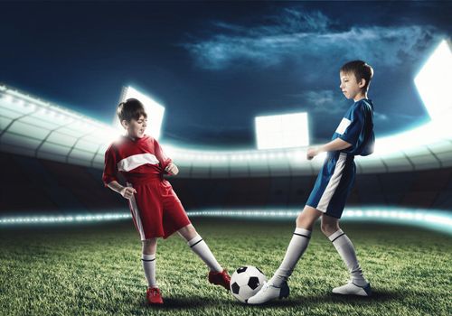 Two boys of school age playing football on stadium