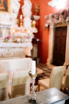Candle in a silver candlestick stands on the table near the altar in the church. High quality photo