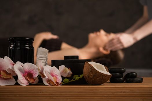 Beautiful woman getting head massage in spa orchid flowers coconut and stones
