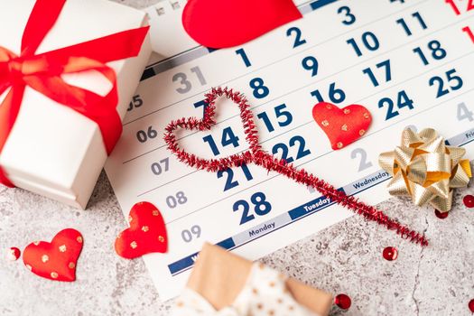 Flat lay of Valentines day calendar composition. Top view Gifts, paper, hearts confetti, ribbon on grey table background. 14th February love concept.