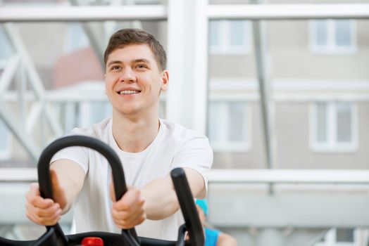 Young guy exercising on bike in fitness center