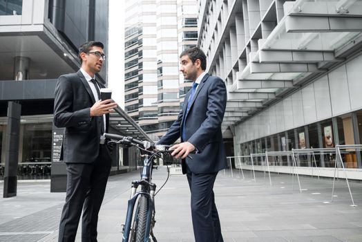Businessmen talking while walking with bicycle outdoors