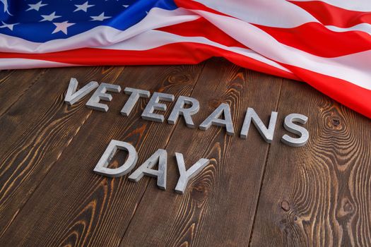 the words veterans day laid with silver metal letters on wooden board surface with crumpled usa flag at upper side with diagonal perspective.
