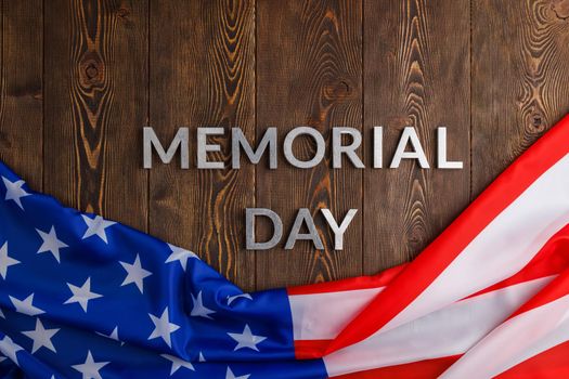 the words memorial day laid with silver metal letters on wooden board surface with crumpled usa flag.