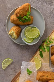 Meat croquets with rosemary leaves and lemons on wooden cutting board in a kitchen counter top.