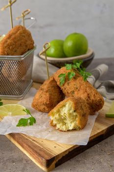 Meat croquets with rosemary leaves and lemons on wooden cutting board in a kitchen counter top.