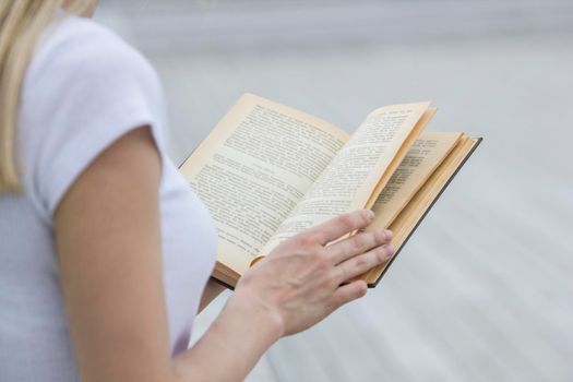 Young female hand holding an old book - reading outdoors, close up