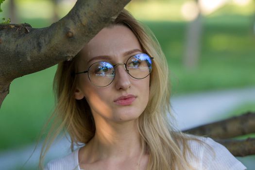 Portrait of young beautiful woman in eyeglasses through the tree branch in the park, horizontal