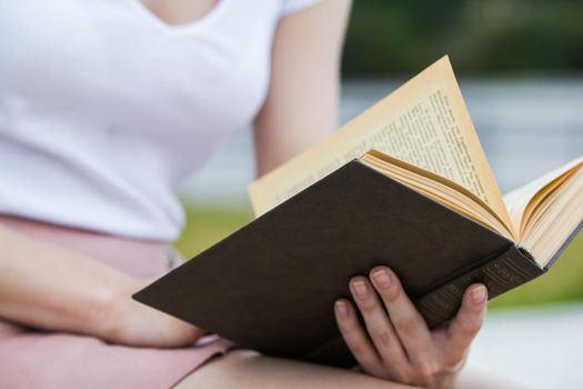 Young woman holding an old book in her hands outdoors, close up