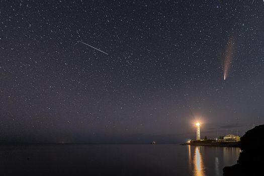 Panoramic HDR Landscape view of Neowise comet over white Lighthouse at night sky. High quality photo