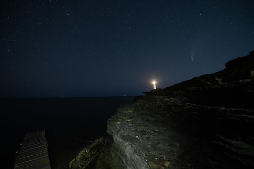 Panoramic HDR Landscape view of Neowise comet over white Lighthouse at night sky. High quality photo