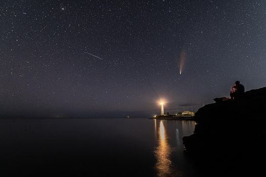 Panoramic HDR Landscape view of Neowise comet over white Lighthouse at night sky. High quality photo