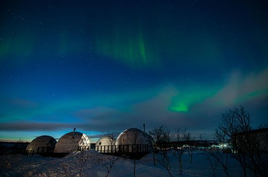 Northern Lights also known as aurora, borealis or polar lights at cold night over igloo village. Beautiful night photo of magic nature of Teriberka, Murmansk. High quality photo