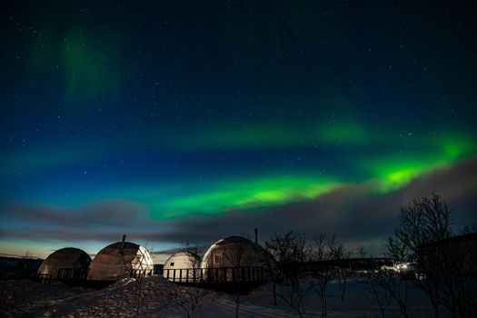 Northern Lights also known as aurora, borealis or polar lights at cold night over igloo village. Beautiful night photo of magic nature of Teriberka, Murmansk. High quality photo