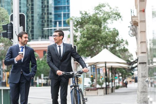 Businessmen talking while walking with bicycle outdoors