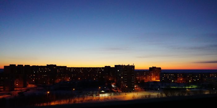 SEVERODVINSK, RUSSIA - MARCH, 11, 2021: Bright winter sunset against the background of houses. Multi-story houses in the rays of the sun. The sun goes down behind the houses