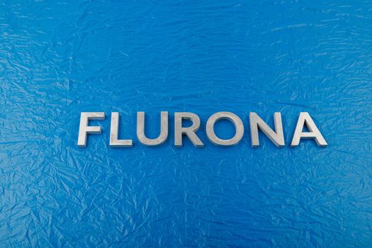 the word flurona laid with silver metal letters on blue crumpled plastic film background, real life photo for flu plus covid concept in frontal perspective view