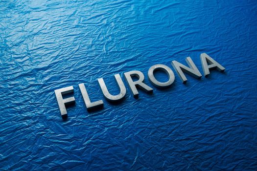 the word flurona laid with silver metal letters on blue crumpled plastic film background, real life photo for flu plus covid concept in diagonal perspective view with dramatic light