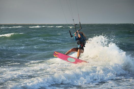 Professional kitesurfer caucasian woman rides big waves in windy weather. Kitesurfing.