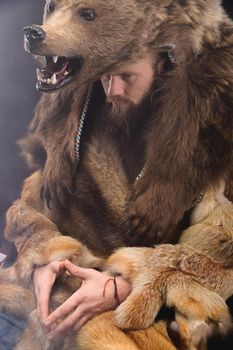 A bearded shaman is sitting dressed in skins, looking thoughtfully aside. Magic in business.