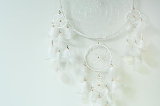 White dreamcatcher hanging on white wall background. handmade willow hoop woven net decorated with feathers. protective charm for infants