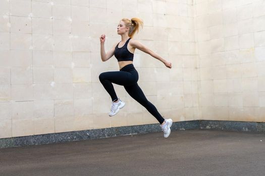 Sport and Fitness Concept Young Adult Caucasian Female Athlete Jumping High Outdoor Gray Tail Wall Background Sportive Woman Jump Exercises Outside Healthy Lifestyle Motivation