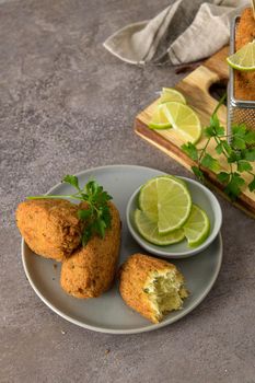 Cod dumplings, or "bolinhos de bacalhau" and parsley leaves and lemons on wooden cutting board in a kitchen counter top.