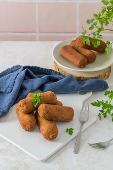 Meat croquets and parsley leaves on white ceramic dishes in a kitchen counter top.