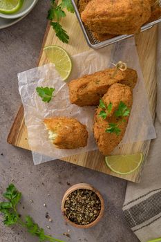 Cod dumplings, or "bolinhos de bacalhau" and parsley leaves and lemons on wooden cutting board in a kitchen counter top.