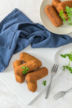 Meat croquets and parsley leaves on white ceramic dishes in a kitchen counter top.