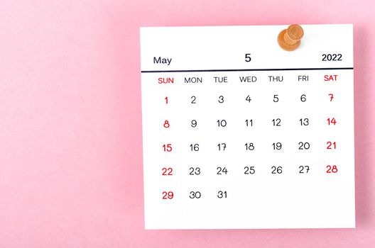 The May 2022 calencar and wooden push pin on pink background.