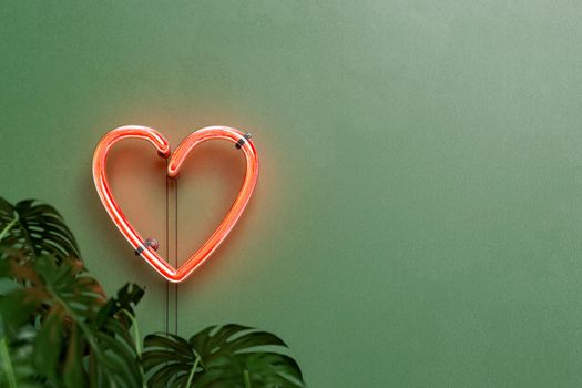 red neon lamp in the shape of a heart on a green wall with plants in front and space for text. valentine's day concept, greeting card, decoration and home. 3d rendering