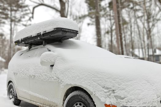 White station wagon covered in deep snow. Car has a roof rack with cargo box that is also covered in snow.