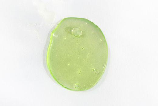 A drop of green hyaluronic acid on white background. Cosmetics and healthcare concept closeup. Dose of serum or retinol with air bubbles. Top view. Luxury gel or beauty product presentation, macro