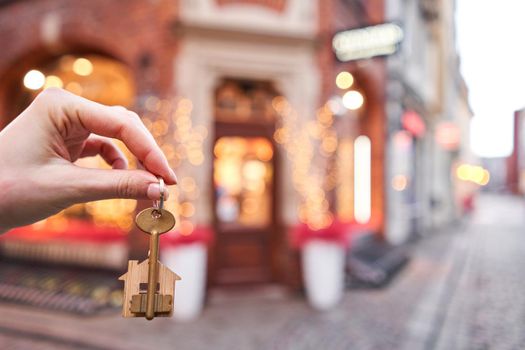 Mortgage or rent concept. Woman holding key with wooden house keychain . Real estate, hypothec, moving home or renting property. Christmas mood in blurred background.