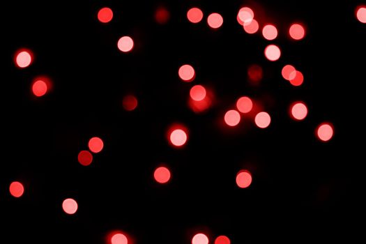 Defocused bokeh lights on black background, an abstract naturally blurred backdrop for Valentine's Day or birthday party. Festive light texture. Pink and red garland in blur. Overlay effect for design