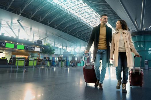 Beautiful couple in love smiles, laughs, enjoys a joint journey, walks through the departure-arrival hall, waits for customs and passport control at the international airport. Airplane travel concept