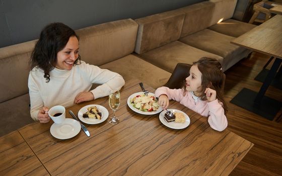 Mother and daughter having lunch together at a restaurant in the airport departure terminal while waiting to board the flight. Beautiful woman travels with her adorable little girl, having a snack