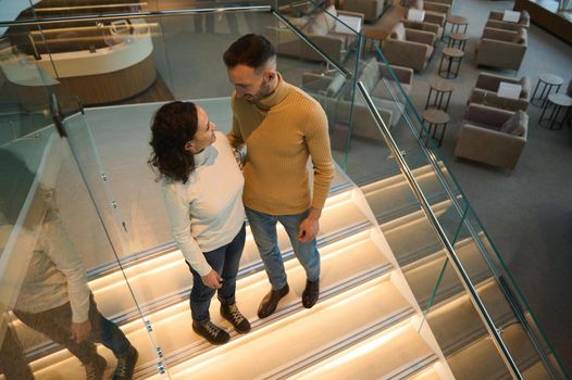 Beautiful happy loving couple stands on the stairs of a lounge zone in an international airport, hugging each other, talking together, waiting for board the flight while travelling on their honeymoon