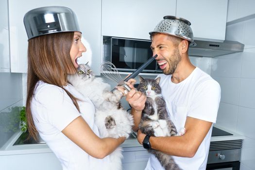 Man and woman funny fighting in the kitchen with their lovely cats. Young couple having fun at home. Couple playing with funny pets. High quality photo