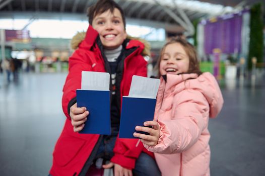 Soft focus on passport document with air tickets and boarding pass in outstretched hands of two adorable European children smiling toothy smile standing at international airport. Family travel concept
