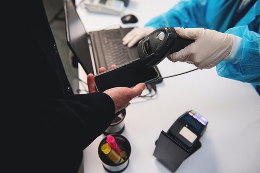 Close-up of a medical health care worker in protective clothing using scanner checking information from a mobile application on a smartphone phone about a traveler's health at international airport