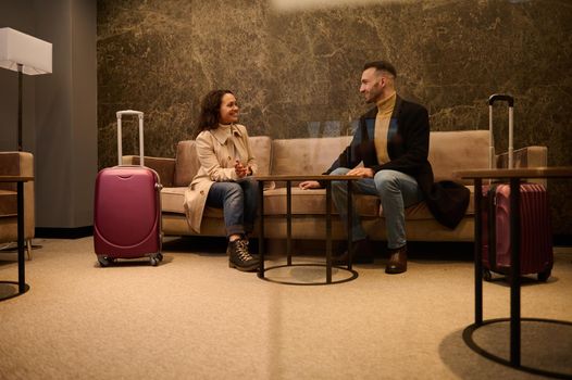 Middle-aged handsome man and pretty woman with suitcases, business partners on a business trip having a conversation in a meeting room while waiting for flight in the airport departure terminal