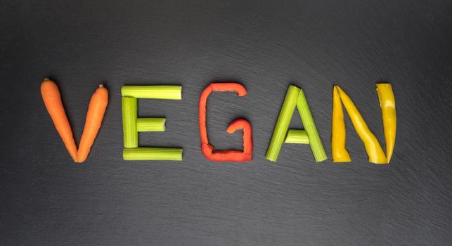 Vegan food and vegan diet concept. Word vegan written with vegetables on black background. High quality photo