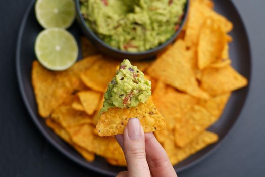 Top view of woman hand holding tortilla chips or nachos with tasty guacamole dip. High quality photo